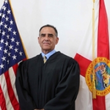 10th Circuit Judge Peter F. Estrada standing in front of the American Flag (on his right) and the State of Florida flag (on his left).
